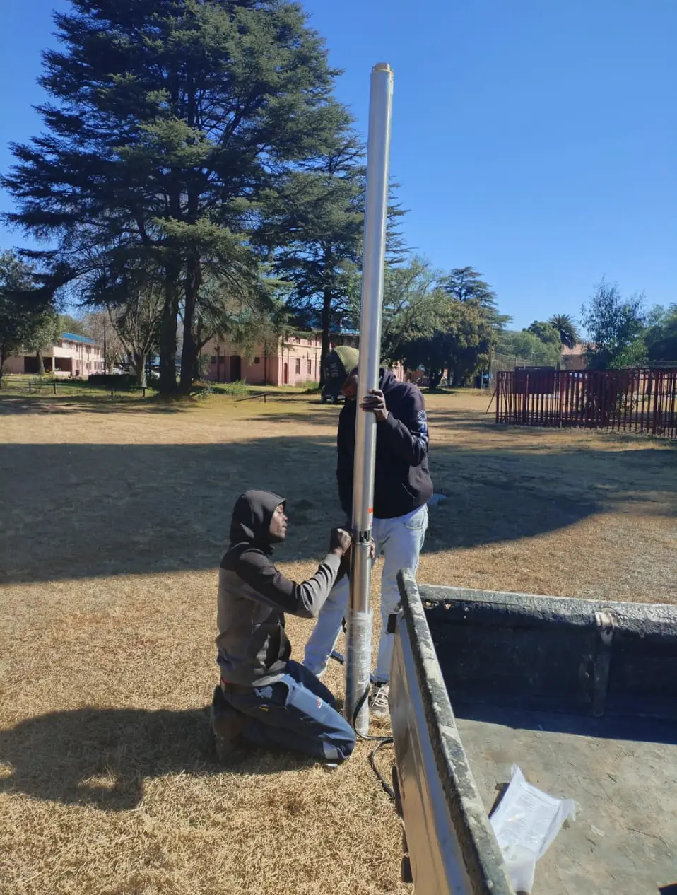 Two borehole drilling installers, working on a borehole pump installation in a field